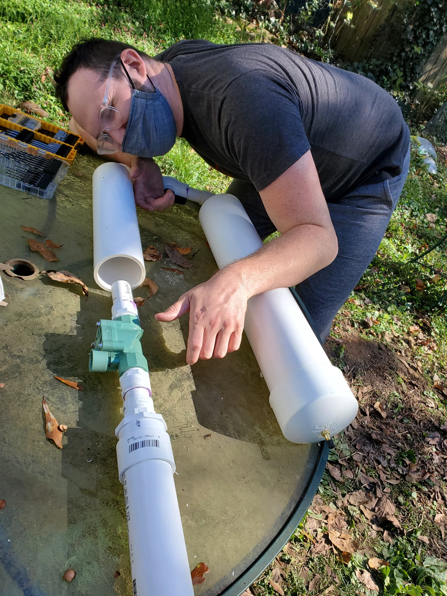 Man crouched over PVC pipe cannon on table with hands on imaginary grip