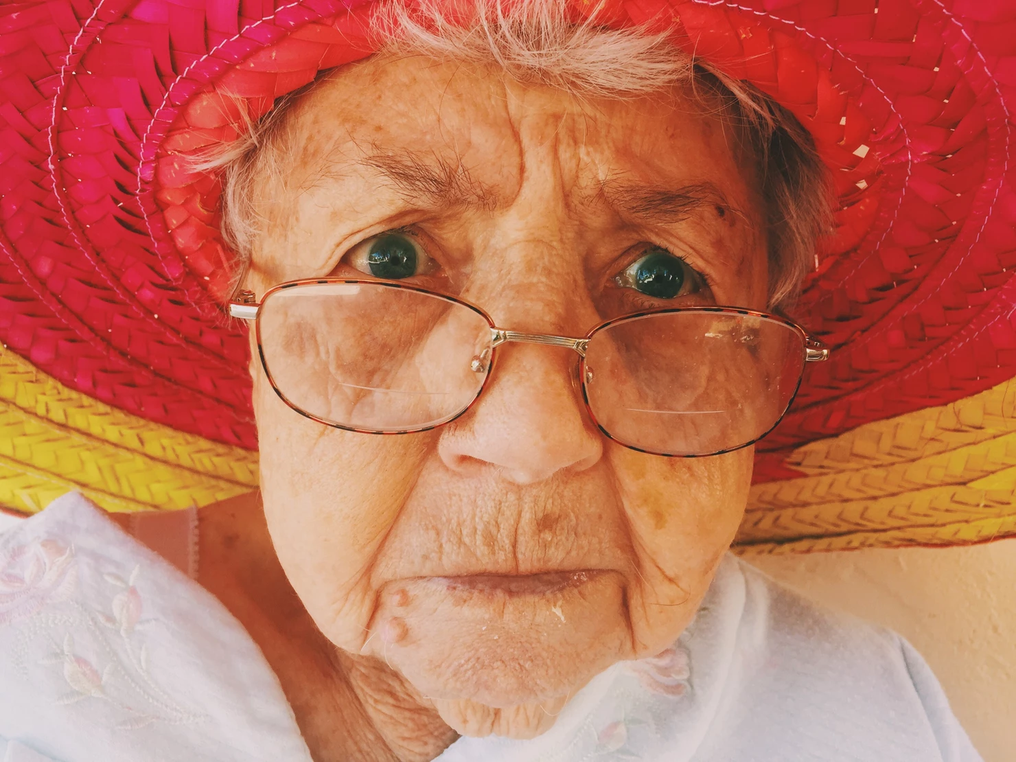 Elderly woman with red and yellow hat and glasses looking worriedElderly woman with red and yellow hat and glasses looking worried