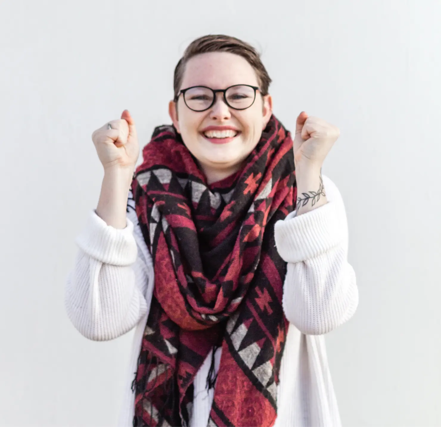 Woman in scarf and glasses and sweater smiling and raising arms in an excited pose